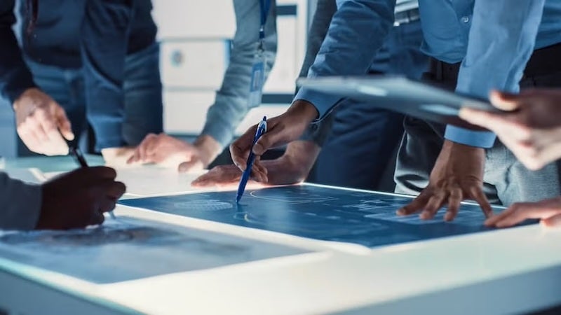 A close-up of professionals analyzing blueprints on a lit surface, symbolizing the critical thinking and planning involved in CTO career progression.