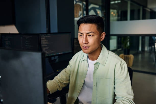 Asian man sitting behind desktop monitor with an engaged expression