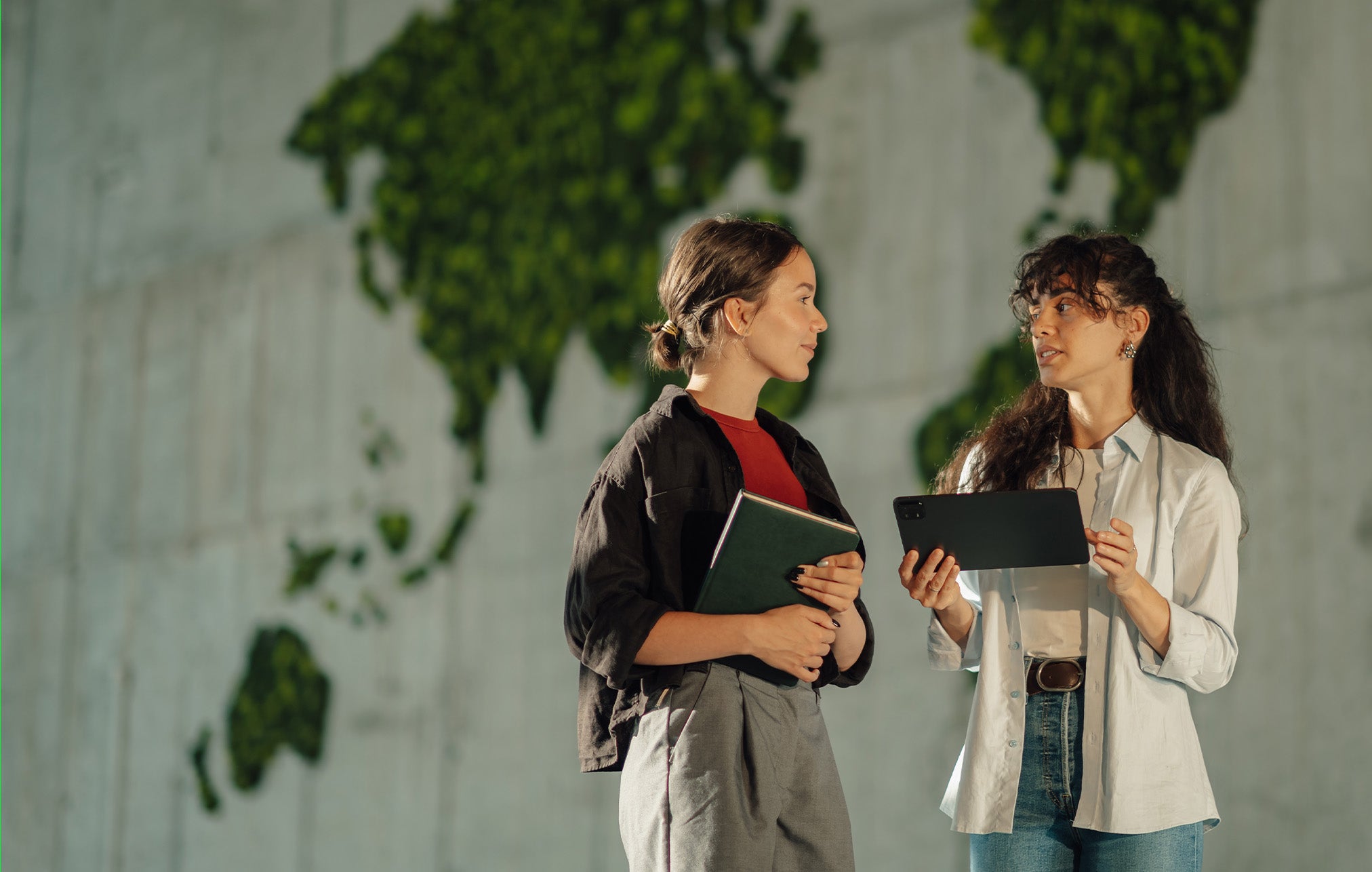 1. Two women stand side by side, each holding a laptop, engaged in conversation or collaboration.