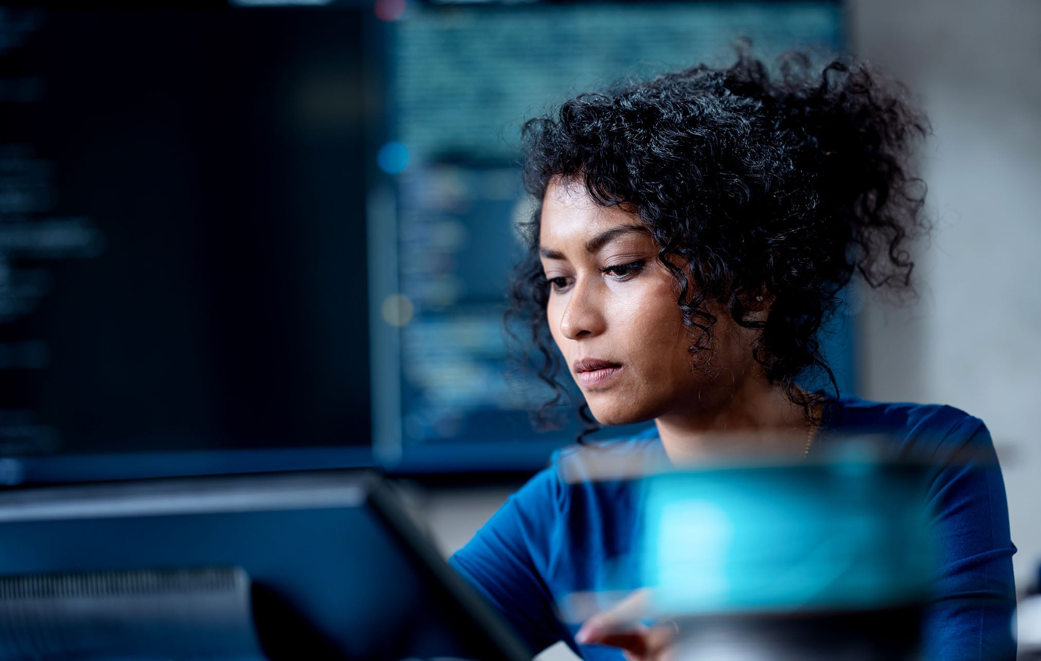 1. A woman in a blue shirt gazes intently at a computer screen, focused on her work.