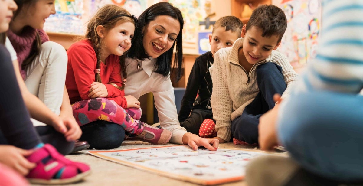 Happy teacher teaching group of small kids in a preschool.