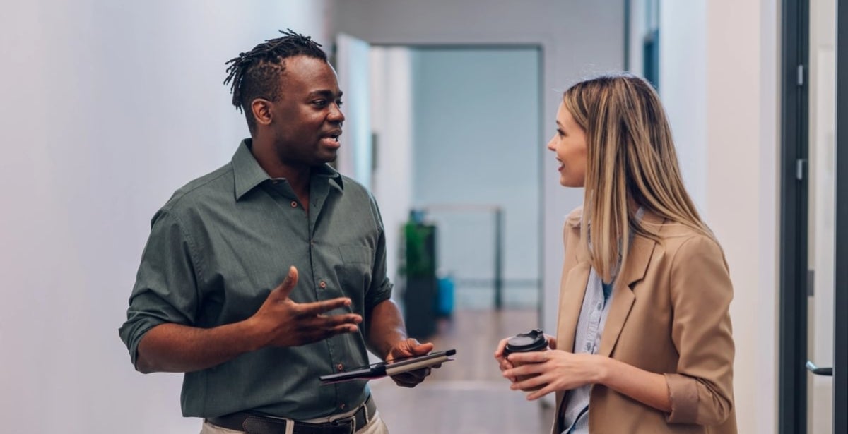 Two business colleagues working together on a digital tablet while standing in a hallway of the office building.