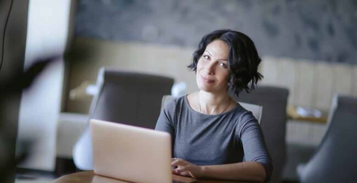 Woman in grey top smiling while using a laptop