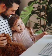 A man holding his daughter while working on a computer, illustrating the challenge of balancing study and life.