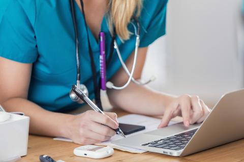 Unrecognizable Caucasian nurse writes something while using a computer in a doctor's office or hospital.