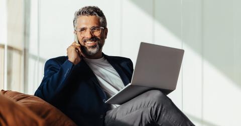 1. A bearded man wearing glasses sits on a couch, focused on his laptop.
