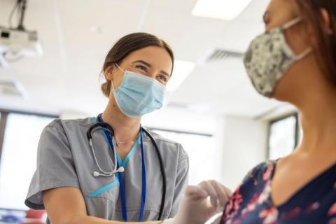 A nurse wearing a mask and gloves is giving an injection to a patient in a healthcare environment.