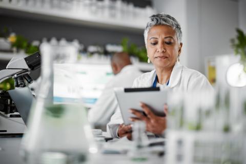 A health data analyst in a lab is using a tablet to review and analyse health information.