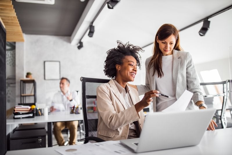 A general manager and a colleague focused on a laptop in an office, engaged in a business discussion.