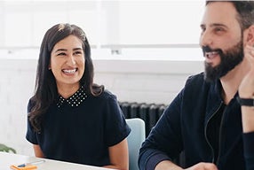 A man and woman seated at a table, focused on a laptop in front of them, engaged in discussion or collaboration.