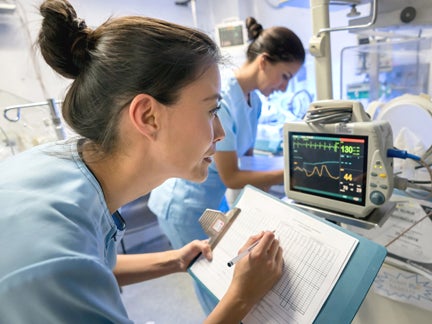 Two nurses collaborating in an intensive care unit, focused on patient care and monitoring medical equipment.