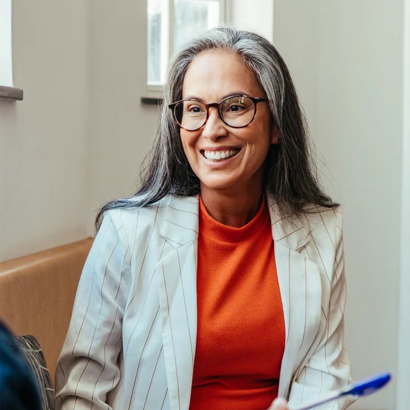 1. A woman wearing glasses and a red shirt smiles warmly at the camera.