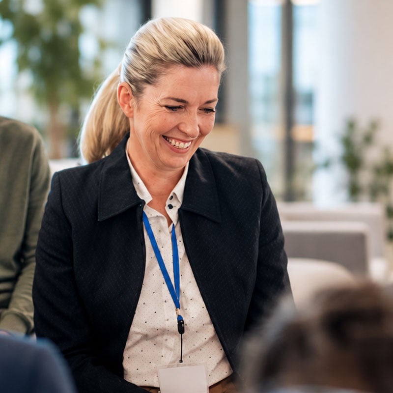 1. A woman smiling while seated at a meeting table, engaged in discussion with colleagues.