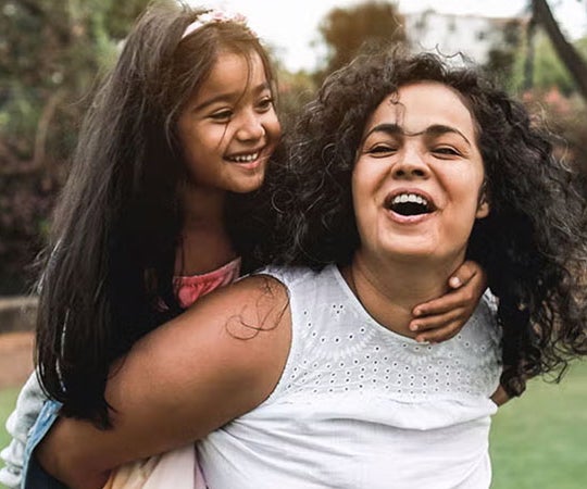 A woman and a young girl share a joyful moment, smiling and laughing together in a warm, friendly atmosphere.