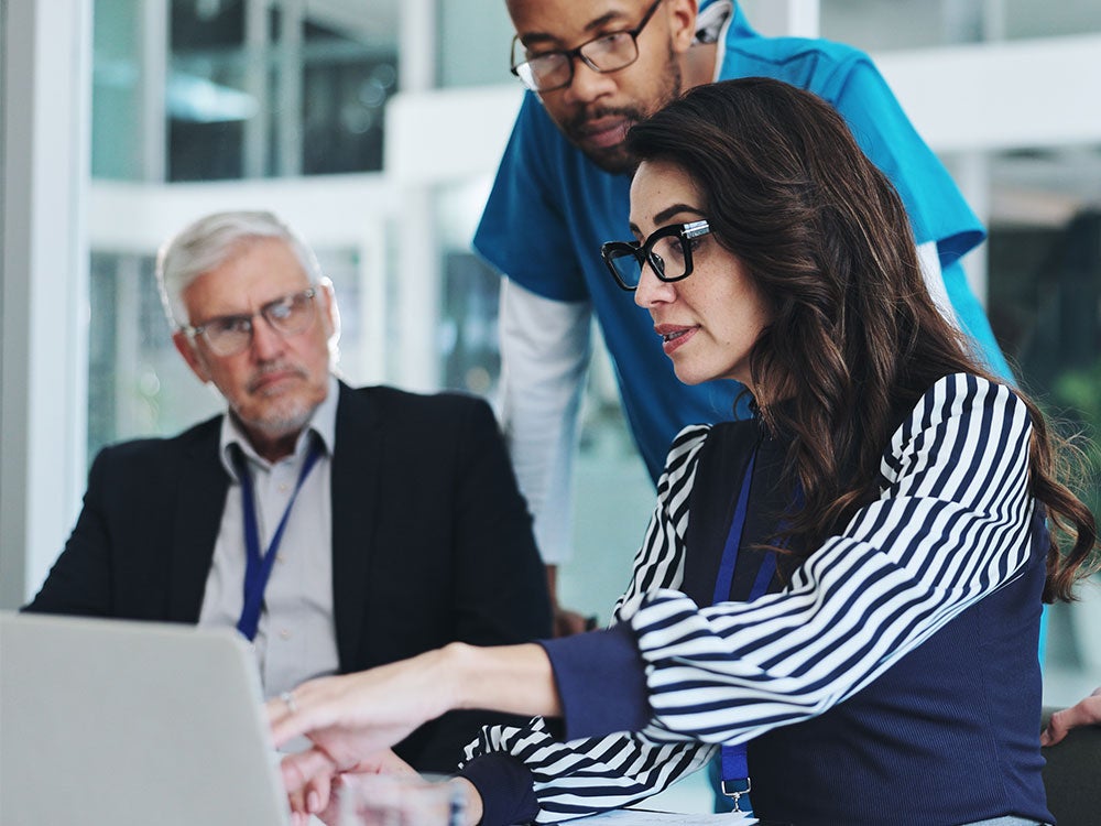 1. Three colleagues collaborating on a laptop in a modern office setting.