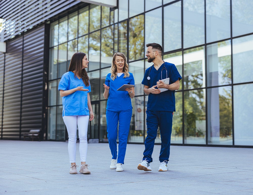 1. Three individuals in scrubs engaged in conversation outside a building.