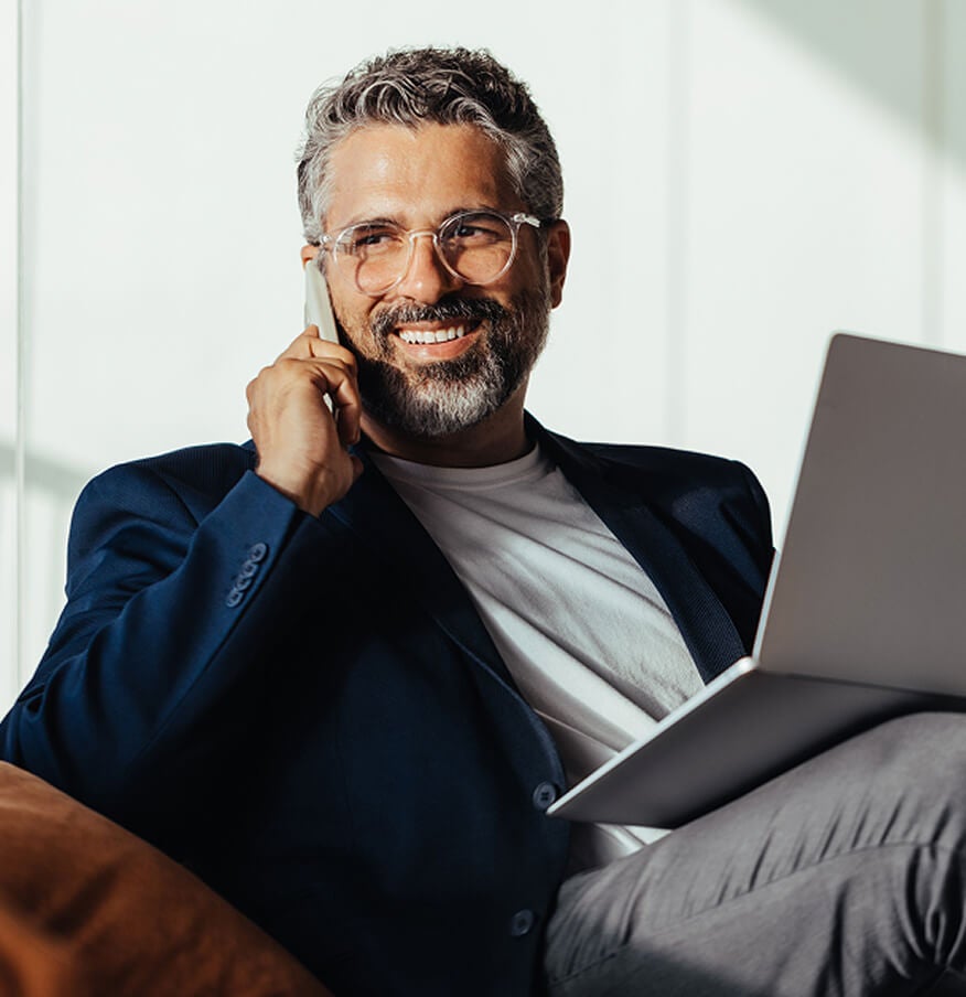 An online MBA student wearing glasses sits on a couch, focused on his laptop.