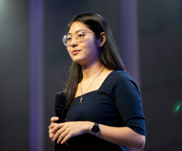 A woman wearing glasses holds a microphone, ready to speak or perform.
