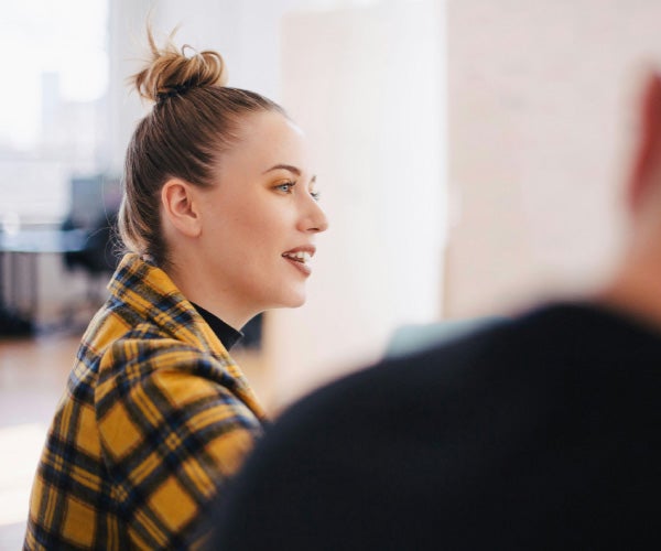 A woman smiles while seated at a desk, working on her laptop, creating a positive and productive atmosphere.