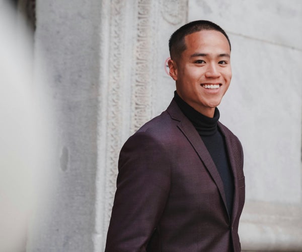 A young man in a suit and tie smiling confidently at the camera.
