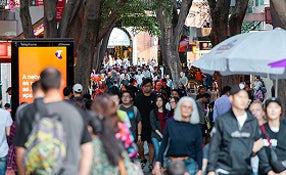 A diverse group of people walking along a busy sidewalk, engaged in conversation and enjoying the day.