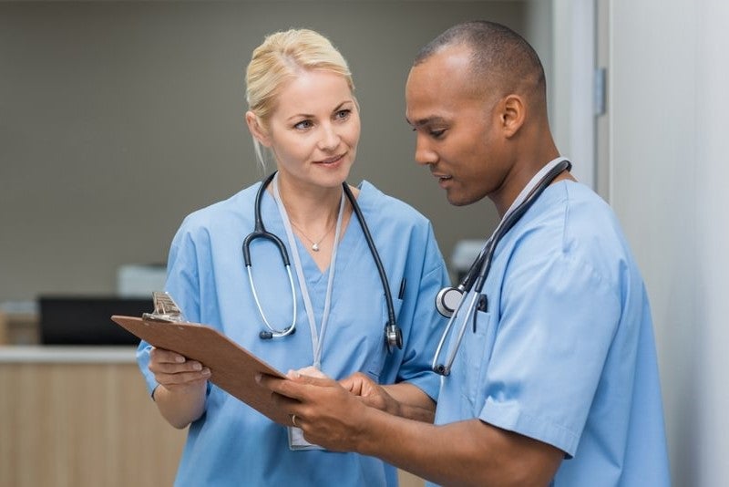 A nurse manager providing guidance to a nurse while they review information on a clipboard.