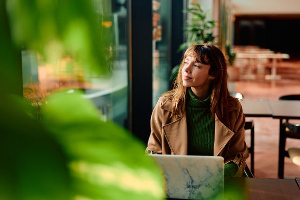 1. A woman seated at a table, focused on her laptop, with a notebook and pen beside her.